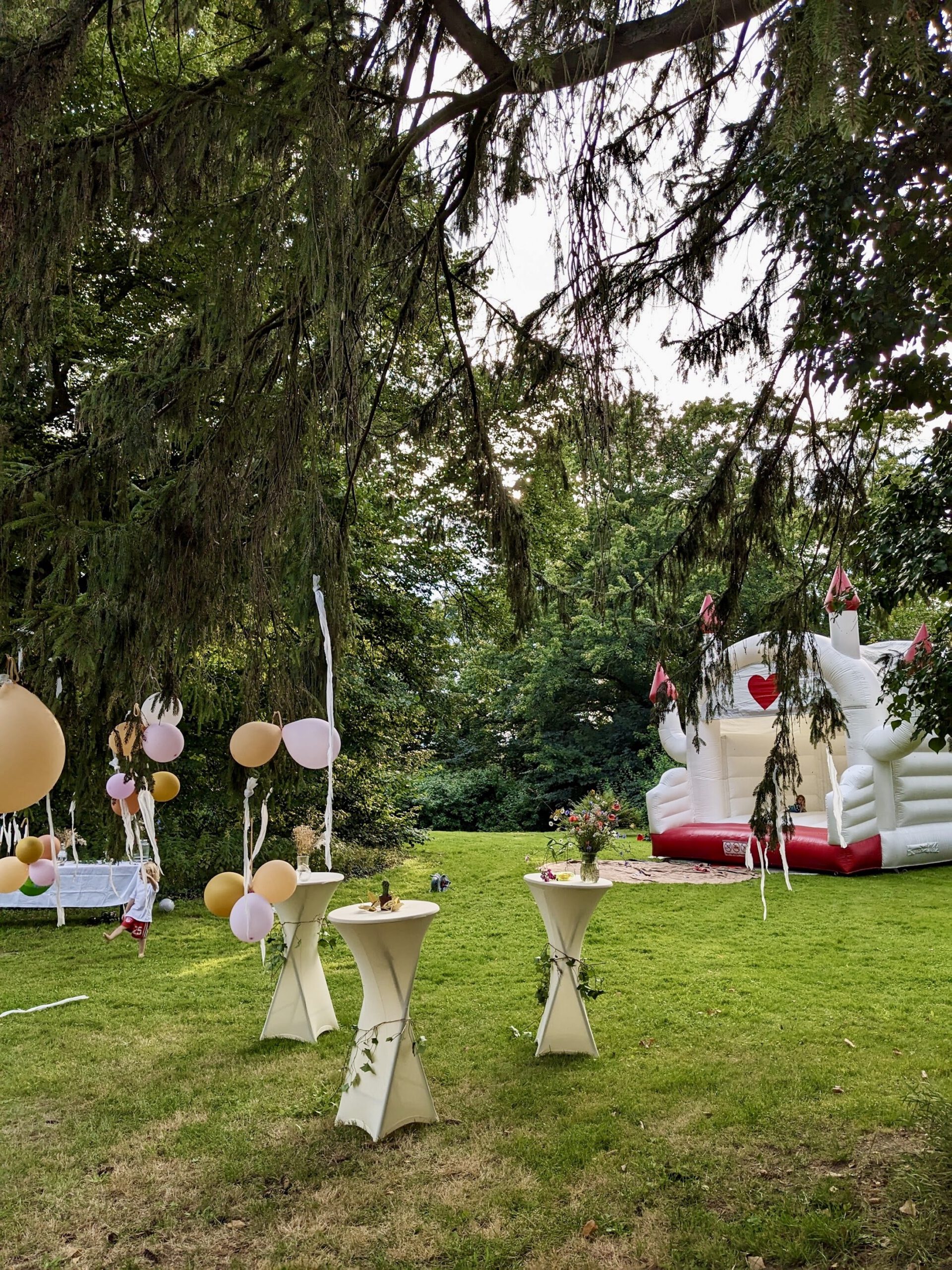 gutshaus-belitz-gartenhochzeit Hochzeitsgarten mit Hüpfburg und Stehtische mit Hussen.