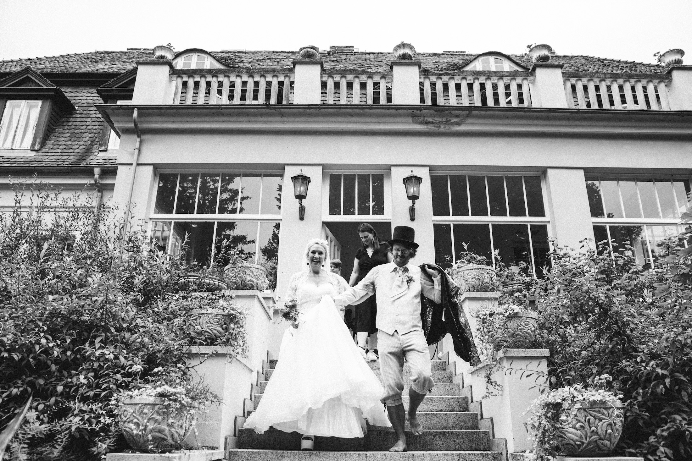 Hochzeitspaar geht die Treppen von Anwesen hinab in Schwarz weiß. 