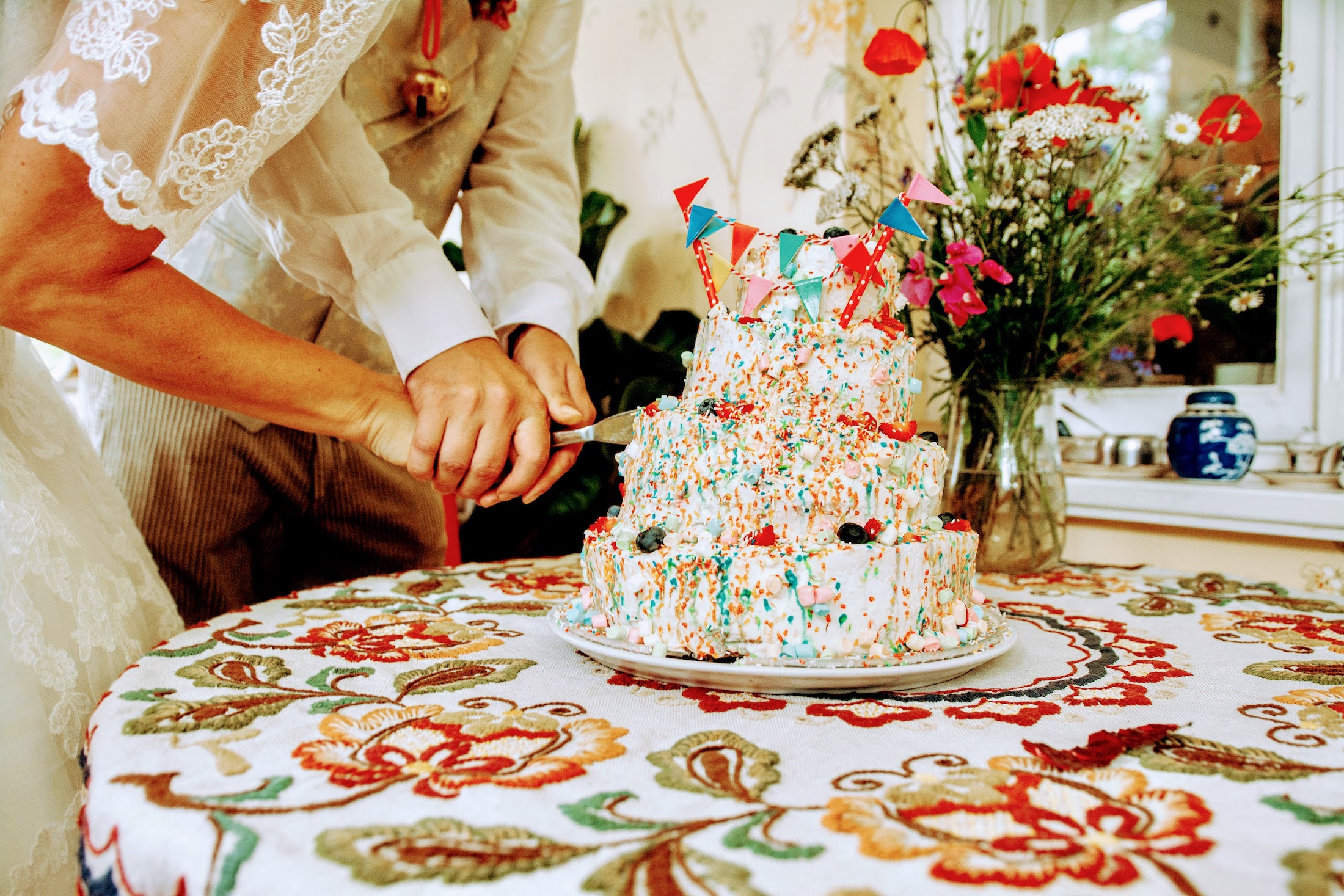 Brautpaar schneidet bunte dreistöckige Hochzeitstorte an.