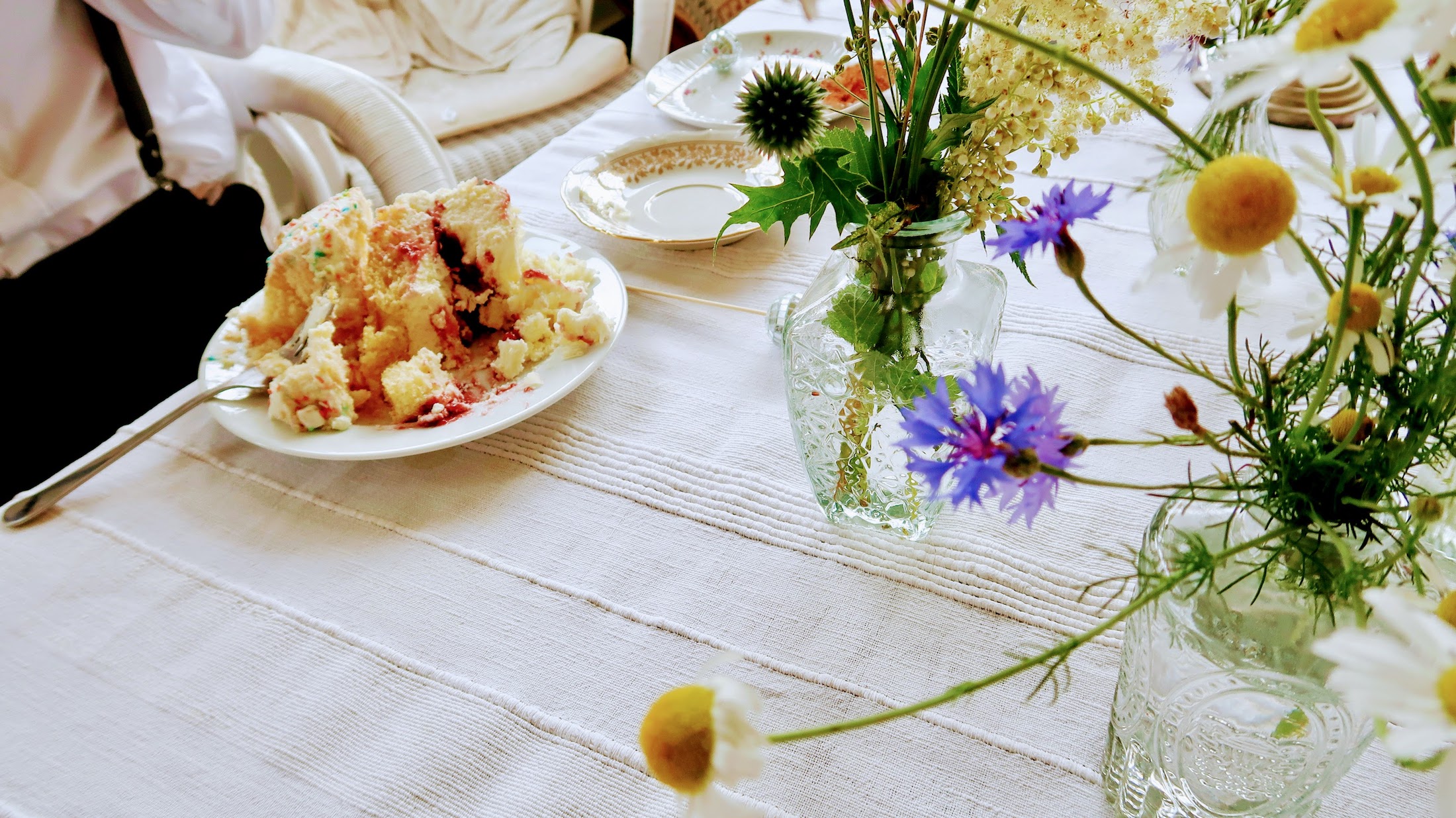 Vollgestopfter Kuchenteller auf weißem Tischtuch mit Wildblumen.