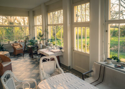 Wintergarten des Gutshauses Belitz mit hellen Möbeln und Blick in den Garten.